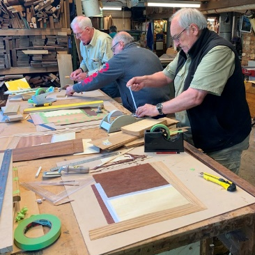Teaser for Veneer Workshop report showing three members preparing some veneers before gluing them to wood