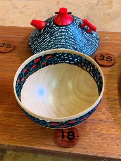 Photo showing a bowl and a teapot. The bowl is light coloured with a ring of dark piercings with some red highlights, while the teapot is blue with red highlights